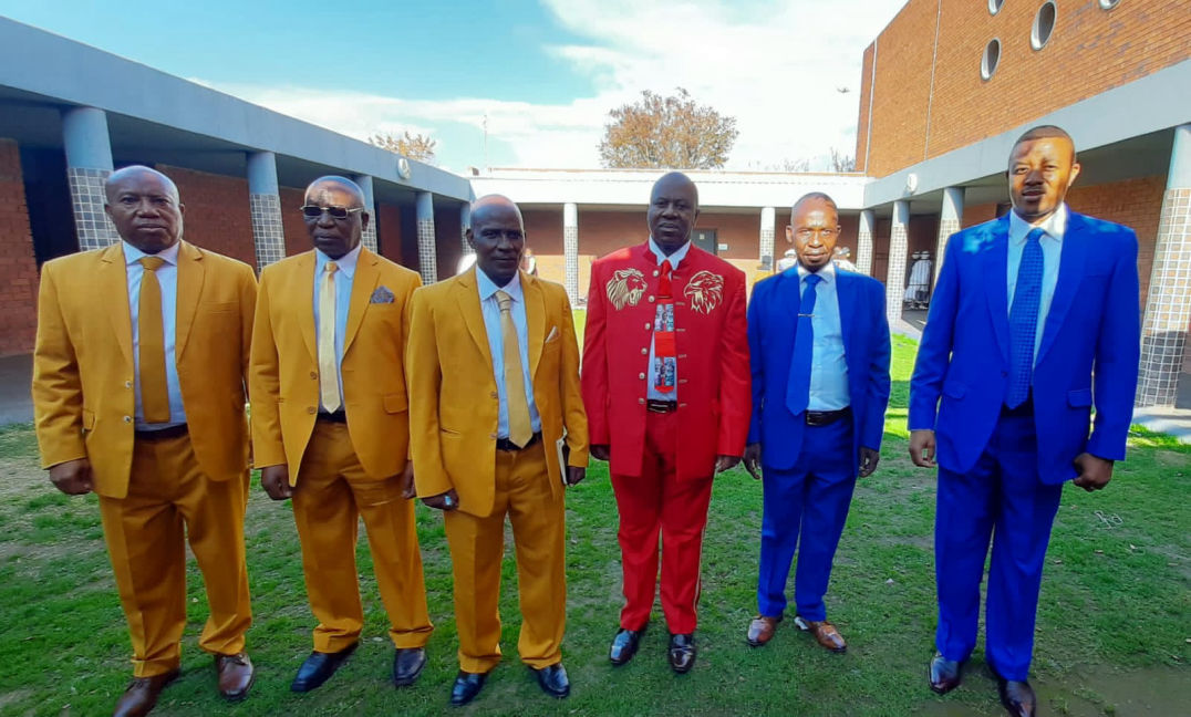 These are the Apostles. On the right with Royal Blue suits.  Apostles Ramafidzha and Apostle Hewu. On the left wearing gold suits it's Apostle Montsho,  Apostle Dube and Apostle Khuzwayo